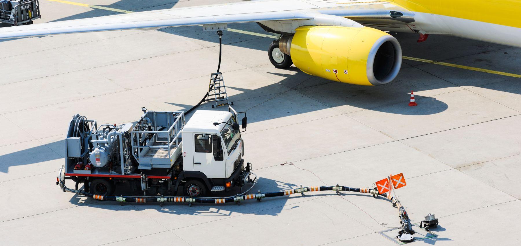 A fuel truck with fuel hose connected to the wing of a passenger jet aircraft.
