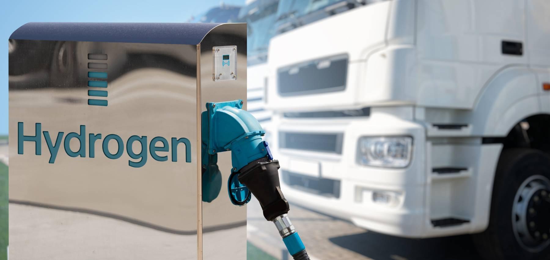 A hydrogen fuel pump bowser with a row of white transport trucks parked in the background