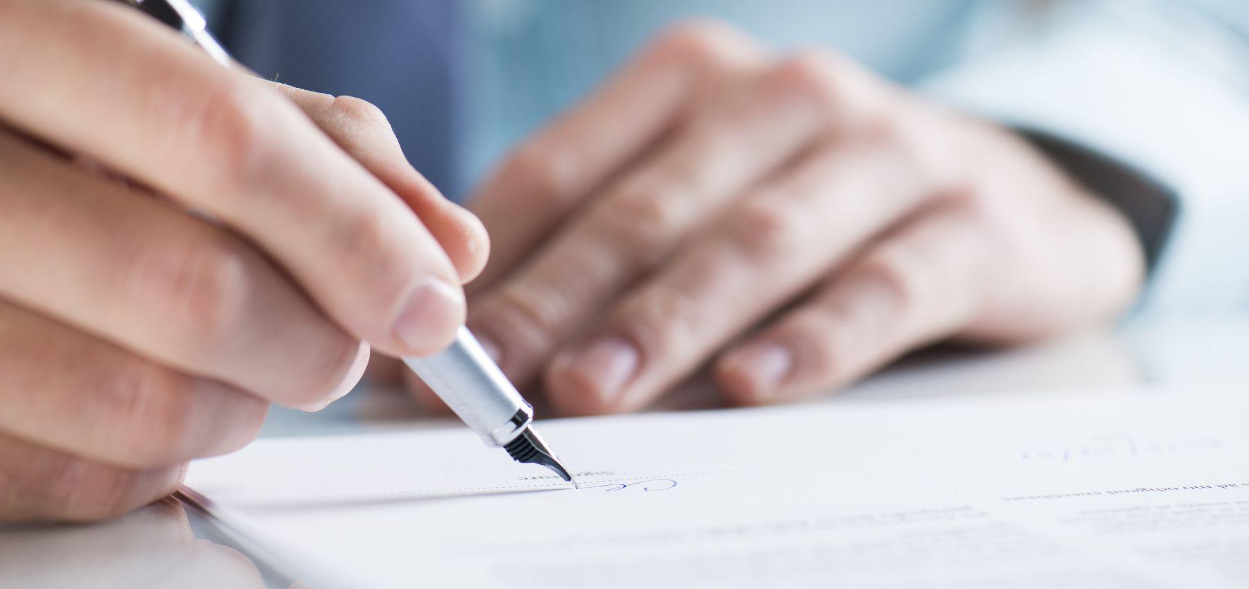 A hand holding a pen signs a document