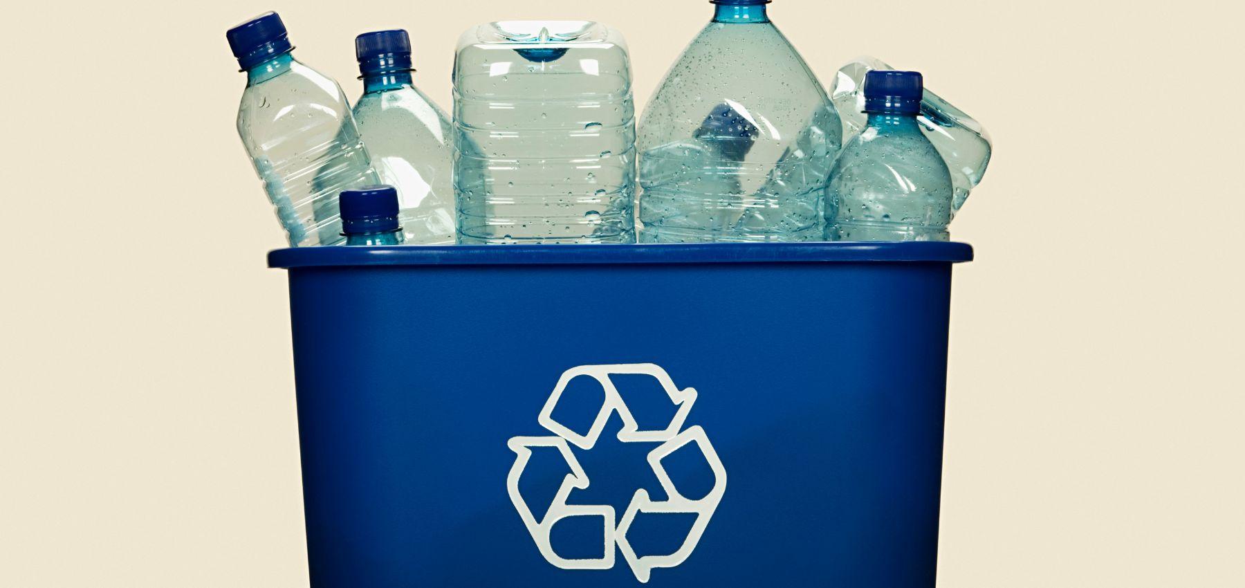 Empty plastic drink bottles sit in a blue recycling bin with recycling triangle symbol on the front