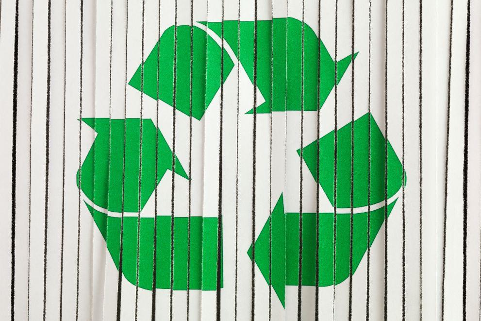 Green arrows of the recycling triangle logo displayed on strips of shredded paper