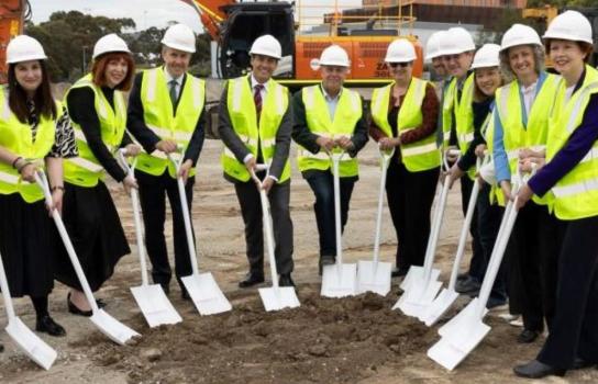 A group of people in safety vests holding spades during a sod-turning ceremony