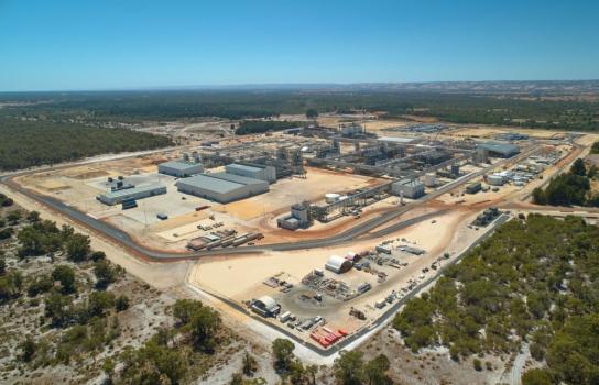 An aerial view of a lithium hydroxide processing plant comprising a large number industrial buildings, roads, pipes and overhead steel walkways.