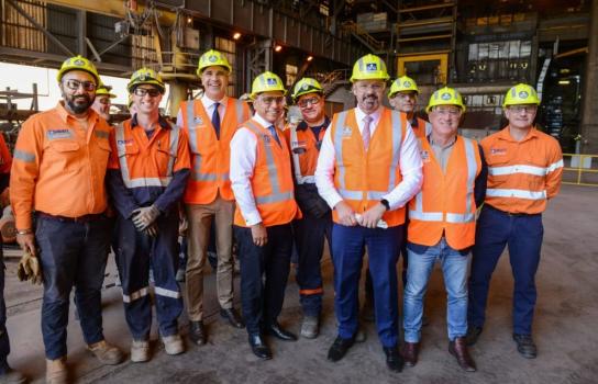 Picture of a group of steel workers wearing orange safety vests and yellow hard hats