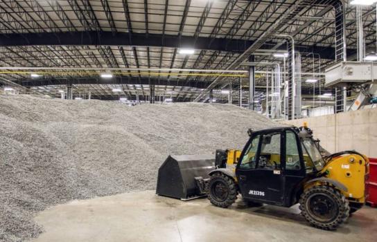 A front end loader is parked next to a pile of processed plastic in a recycling facility